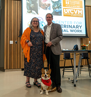 Dean Lori Messinger stands with Dean Jim Thompson who is holding the leash of a Pembroke Corgi wearing a red HABIT scarf.