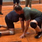 Coach Smith is showing another wrestler a technique on the wrestling mat