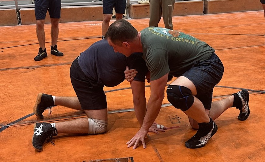 Coach Smith is showing another wrestler a technique on the wrestling mat