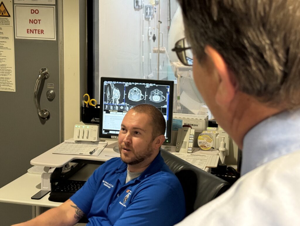 Dr. Plummer is looking at and speaking with an MRI technician wearing blue scrubs