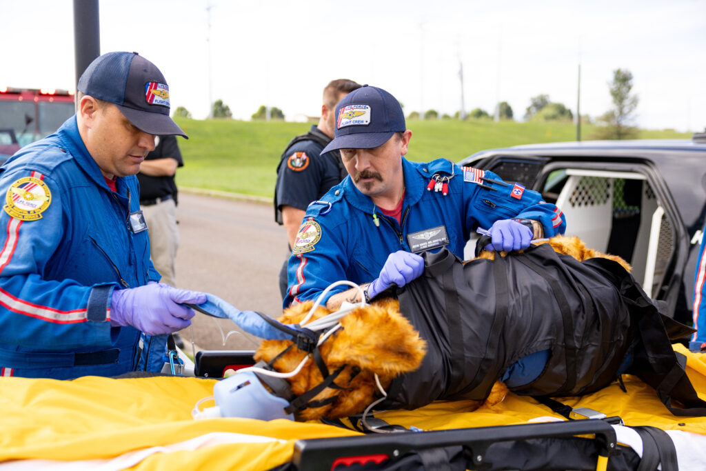 Two flight nurses dressed in blue transfer the model patient into a waiting police cruiser.