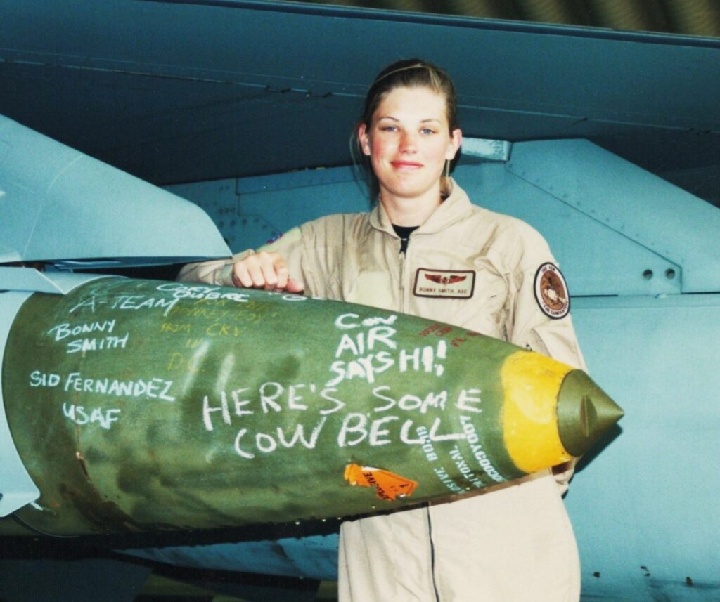 A female soldier in flight uniform stands next to a missile