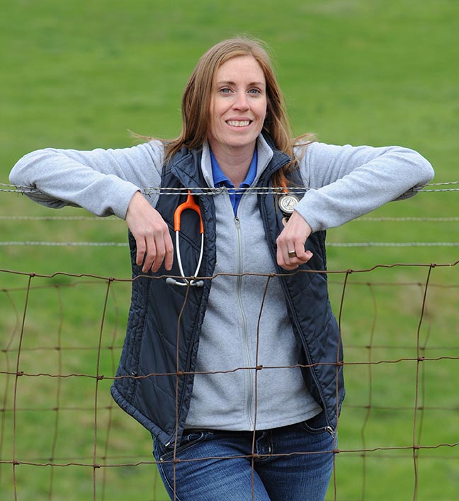 Dr. Andi Lear standing at a fence in a field