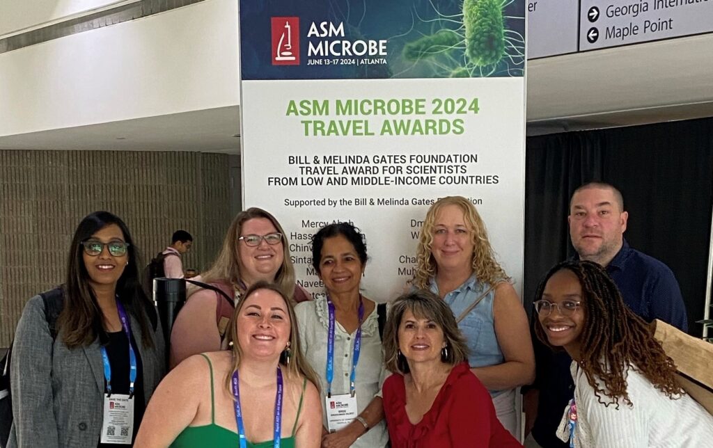 Members of the clinical bacteriology and mycology lab pose for a photo in front of the ASM conference sign