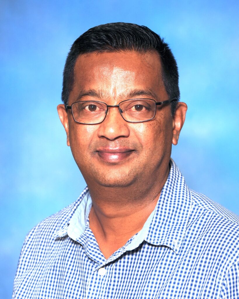 A headshot of Dr. Girish Neelakanta smiling at the camera while wearing a blue and white checked shirt.