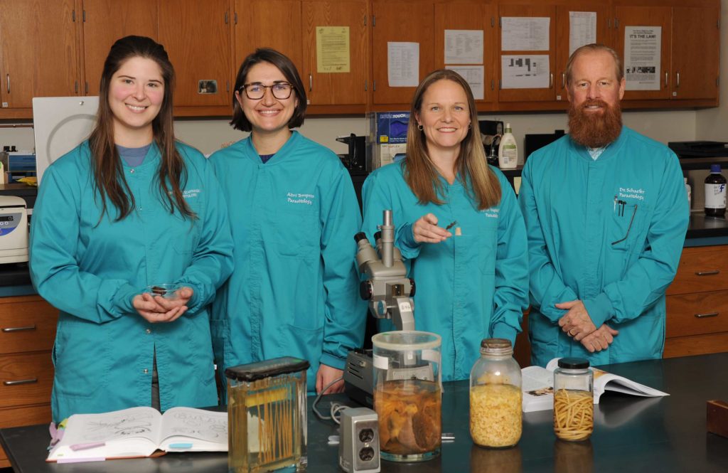 Parasitology lab members stand in blue lab coats with parasite samples
