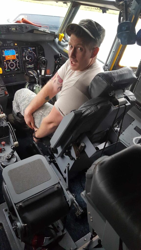 A man in the United States Air Force looks over his shoulder while sitting in the cockpit of a plane