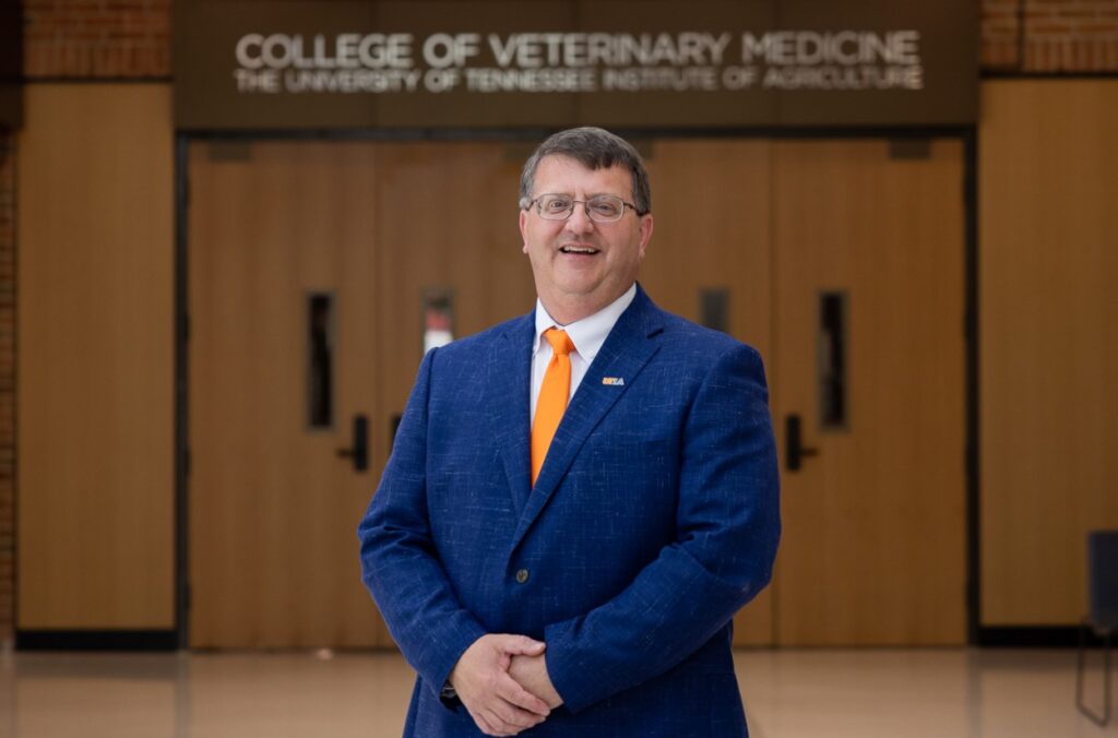 Dean Paul Plummer wearing a blue blazer and orange tie stands in front of a sign that reads college of veterinary medicine the university of tennessee institute of agriculture