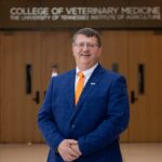 Dean Paul Plummer wearing a blue blazer and orange tie stands in front of a sign that reads college of veterinary medicine the university of tennessee institute of agriculture