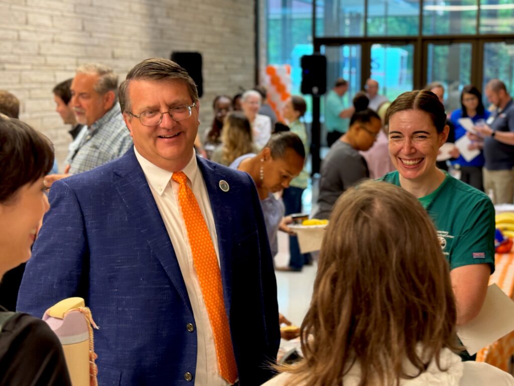 Dr. Plummer, wearing a navy jacket and orange tie talks to veterinary students and faculty during a morning mixer