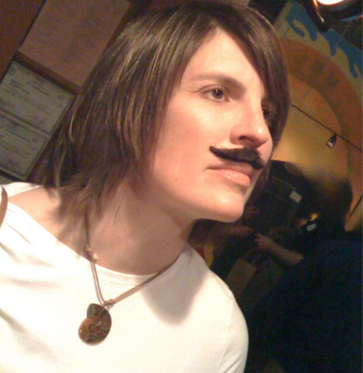 A woman wearing a white shirt looks wistfully toward the ceiling while sporting a face mustache.