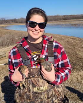 Nicole Szafranski in plaid shirt and overalls standing beside a river