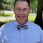 Dr. Brian Whitlock stands outside wearing a light blue shirt and bowtie