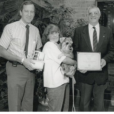 A woman and her dog are presented with a certificate by Dr. D.J. Krahwinkel and Dean Michael Shires. 