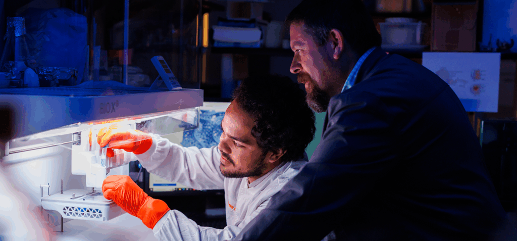 Two researchers looking at lab samples in a test tube in a lab setting.